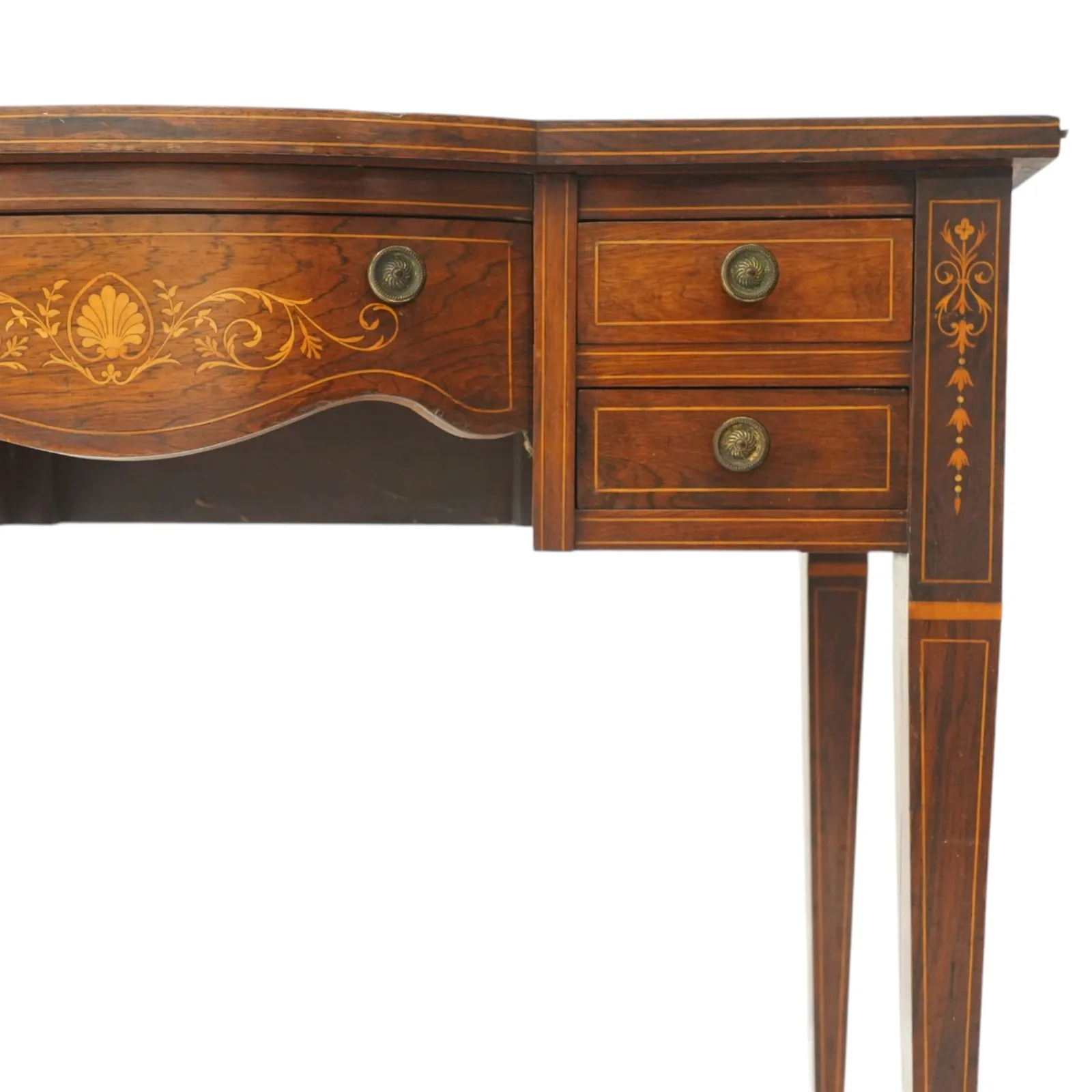 19th century inlaid mahogany bow-front writing table, rectangular shaped top with inset read leather writing surface and satinwood stringing, fitted with single bowfront frieze drawer decorated with scallop shell and trailing foliate motifs, flanked by two drawers to each side, the uprights inlaid with bellflowers, terminating to square tapering supports with ceramic castorsProvenance: Kirkham Hall thumbnail 4