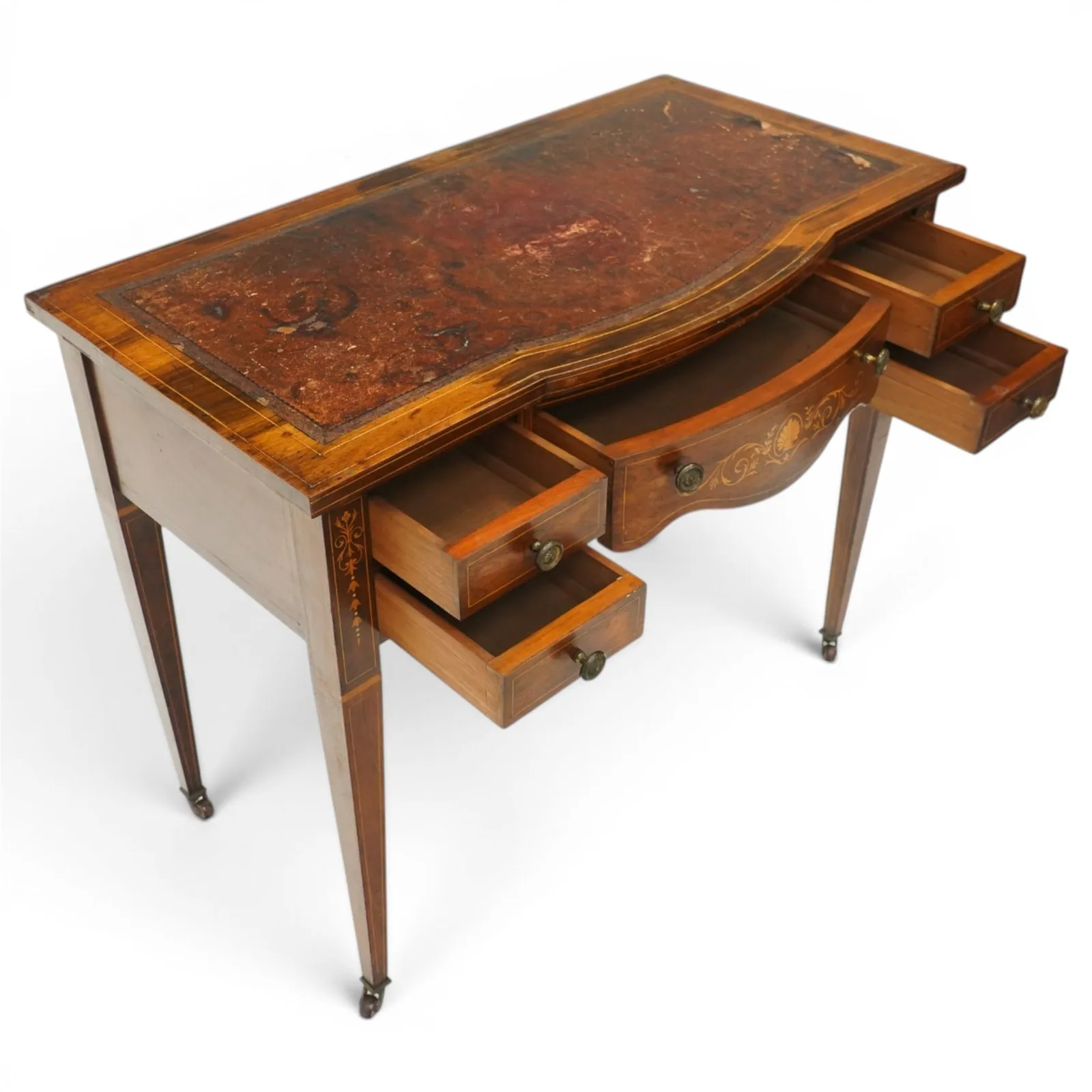 19th century inlaid mahogany bow-front writing table, rectangular shaped top with inset read leather writing surface and satinwood stringing, fitted with single bowfront frieze drawer decorated with scallop shell and trailing foliate motifs, flanked by two drawers to each side, the uprights inlaid with bellflowers, terminating to square tapering supports with ceramic castorsProvenance: Kirkham Hall thumbnail 3