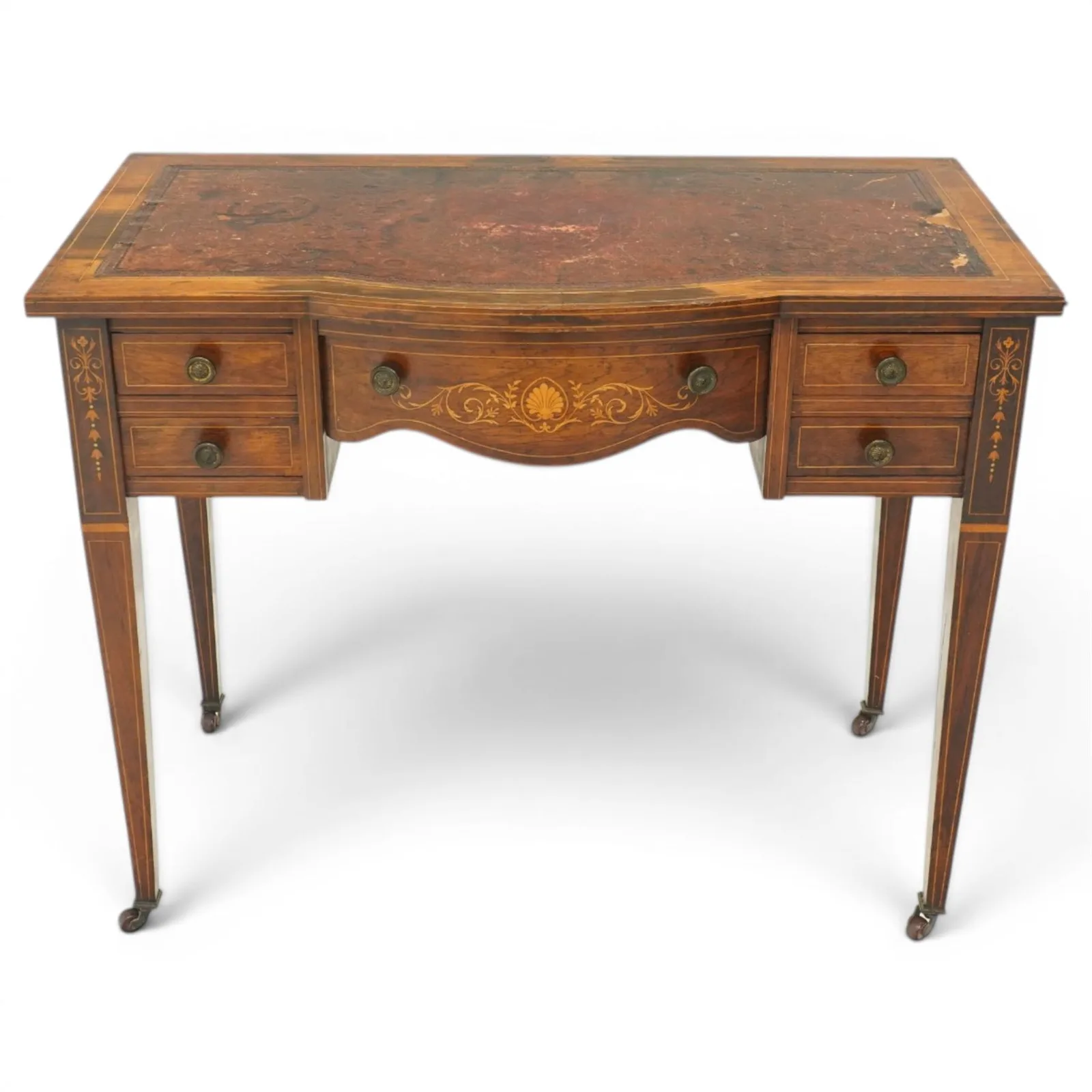 19th century inlaid mahogany bow-front writing table, rectangular shaped top with inset read leather writing surface and satinwood stringing, fitted with single bowfront frieze drawer decorated with scallop shell and trailing foliate motifs, flanked by two drawers to each side, the uprights inlaid with bellflowers, terminating to square tapering supports with ceramic castorsProvenance: Kirkham Hall - Plate 1