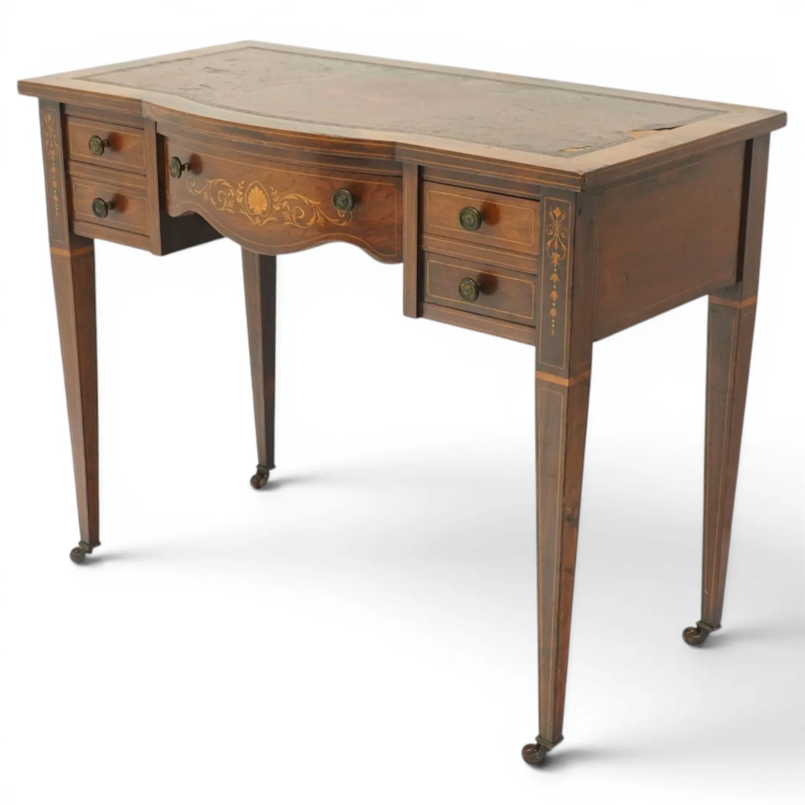 19th century inlaid mahogany bow-front writing table, rectangular shaped top with inset read leather writing surface and satinwood stringing, fitted with single bowfront frieze drawer decorated with scallop shell and trailing foliate motifs, flanked by two drawers to each side, the uprights inlaid with bellflowers, terminating to square tapering supports with ceramic castorsProvenance: Kirkham Hall thumbnail 2
