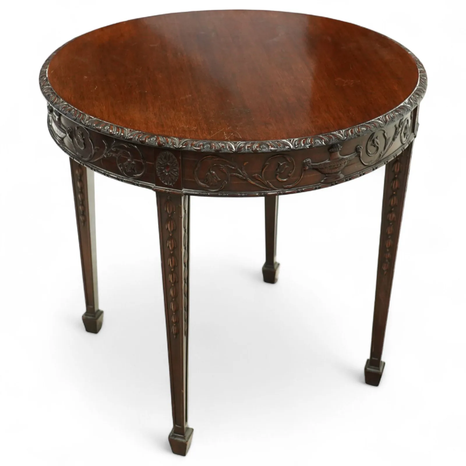 Early 20th-century Adam style mahogany circular centre table; moulded frieze carved with scrolling foliage, urns and rosettes; square tapering legs with husk carving, terminating in spade feet - Plate 1